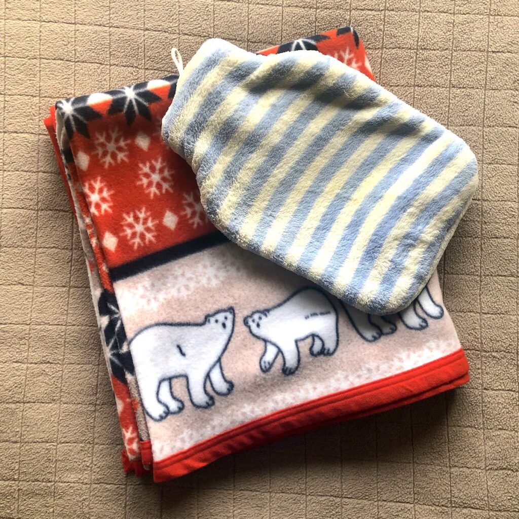 A folded blanket (with polar bears on it) with a blue and white striped hot water bottle on the top of it